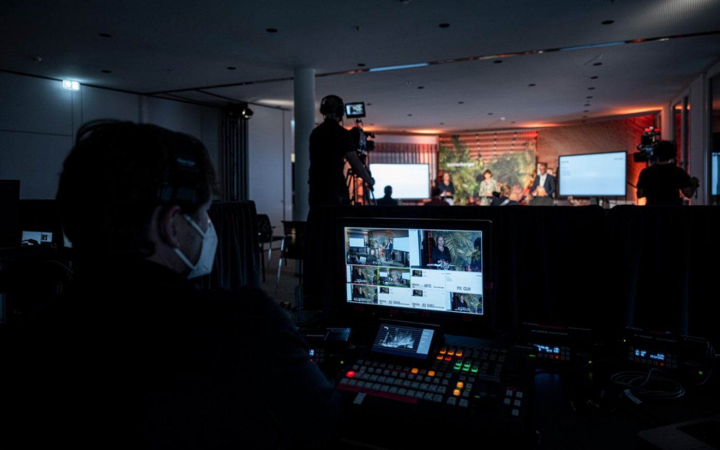 Helena Glantz, Barbara Enzinger and Heimo Scheuch on stage, livestream and cameras on screen